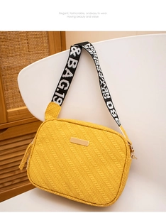 Detail of yellow woven crossbody bag featuring a golden plaque and wide logo strap