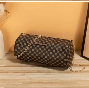 Detail of cylinder crossbody bag with clover print and gold chain on wooden desk