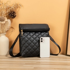 Black quilted crossbody bag with gold zipper and wide strap on an orange background