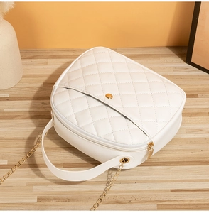 Detail of white quilted handbag with gold chain strap and metal zipper on wooden surface