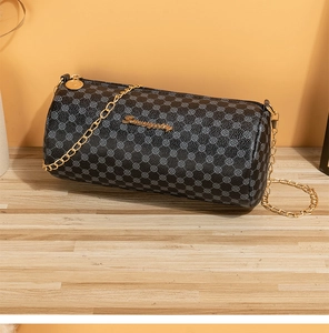Macro shot of black barrel bag with vintage pattern and gold chain strap on wood