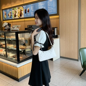 Elegant white quilted rhombus underarm baguette bag worn by a woman in a cafe