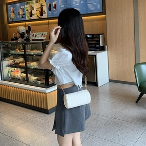 White quilted cylinder bag with metal chain strap worn by a woman in a cafe setting