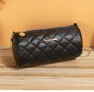 Close-up of black quilted cylinder bag with gold chain strap and metal logo on wood