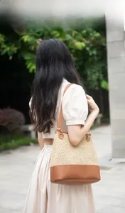 Outdoor view of beige woven bucket bag with brown leather base and long strap on model