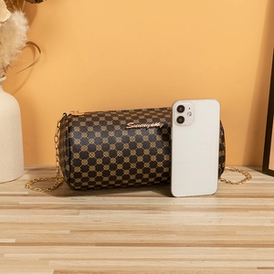 Brown cylinder chain bag with golden floral pattern and metal strap on wooden surface