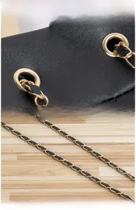 Détail de la ferrure dorée polie et de la chaîne entrelacée de cuir sur un sac seau noir
