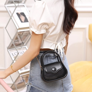 Chic black shiny PVC jelly bag with metal chain strap shown in a stylish indoor setting