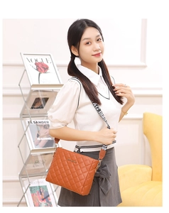 Brown quilted crossbody bag with stylish wide letter strap on a cozy background