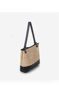 Detail view of woven straw tote bag with black leather base and long shoulder straps