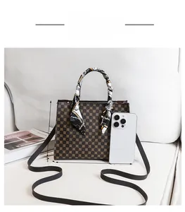 Detailed view of a brown printed handbag with silk scarf and black crossbody strap