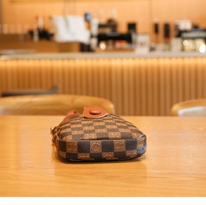 Detail of a mini crossbody bag featuring a classic brown checkerboard pattern on a wooden surface