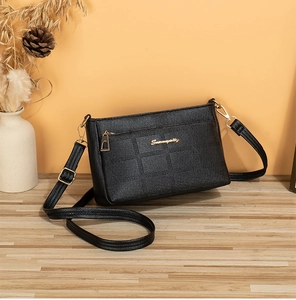 Detail of black pebbled leather crossbody bag with square quilting and gold logo