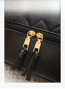 Détail des doubles fermetures éclair dorées et longs tirettes en cuir du sac à dos
