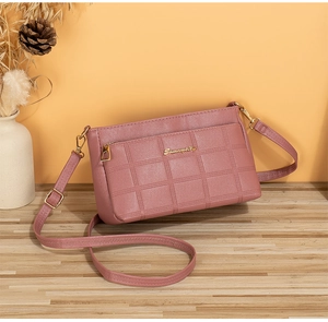 Detail of pink faux leather crossbody bag with square embossed pattern and gold logo