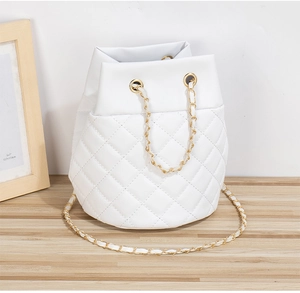 Détail du sac seau blanc matelassé avec bandoulière en chaîne dorée sur bois