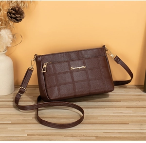 Close-up of brown checkered embossed leather bag with gold logo on a wooden surface
