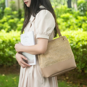 Straw woven tote bag with khaki leather trim worn by model in an outdoor garden setting