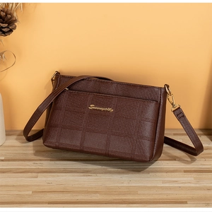 Detailed view of brown embossed leather crossbody bag with golden logo on wooden surface