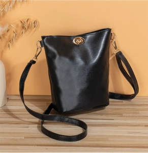 Détail d'un sac seau noir avec un fermoir rotatif doré sur un sol en bois naturel