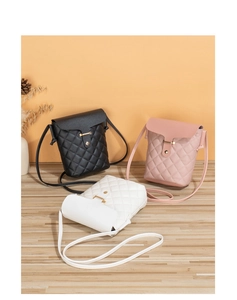 Three quilted mini bucket crossbody bags in black, pink, and white on a wooden floor