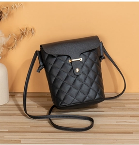 Close-up of a black quilted bucket bag with gold hardware on a wooden table