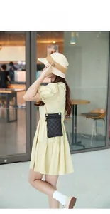 Detail of black quilted leather phone bag with gold chain strap worn by a model