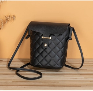 Close-up of black quilted crossbody phone bag with gold hardware on wooden surface