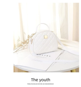 Close-up of white quilted shell crossbody bag with gold hardware on marble surface