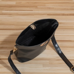 Sac seau noir minimaliste en cuir ciré avec détails dorés sur un parquet en bois