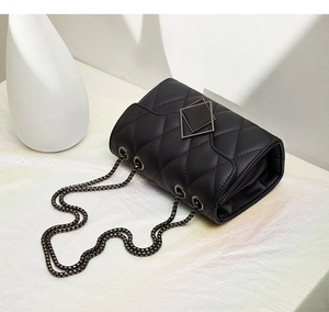 Detail of classic black quilted shoulder bag featuring a geometric metal buckle and chain strap