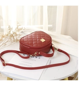 Detail of red heart-shaped quilted leather handbag with gold zipper on a white table