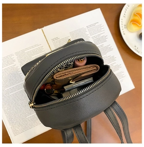 Internal storage view of black pebble leather mini backpack with gold zippers and daily items