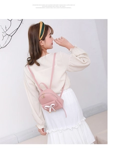 Vue arrière détaillée d'un mini sac à dos en cuir rose avec nœud blanc sur un mannequin