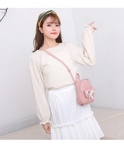 Détail d'un mini sac à dos rose avec nœud blanc porté à l'épaule par un mannequin