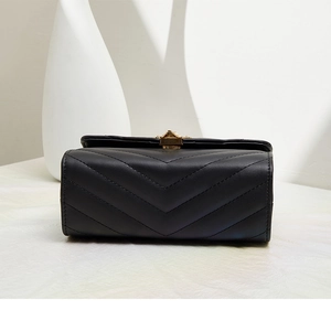 Dettaglio della borsa nera trapuntata a V con elegante chiusura a girello dorata su bianco