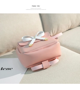 Détail d'un mini sac à dos rose avec un nœud blanc et des finitions métalliques dorées