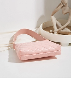 Close-up of pink quilted faux leather shoulder bag with gold metal logo on a white pedestal