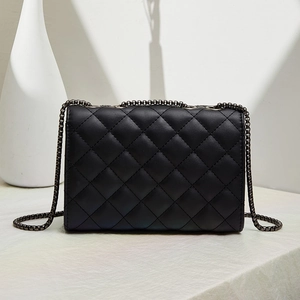 Sac à bandoulière matelassé noir avec chaîne en métal sur fond blanc minimaliste