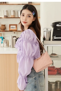 Pink quilted shoulder bag with V-pattern stitching and gold logo in a cafe setting