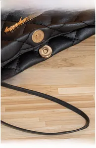 Detail of high-polished gold magnetic clasp on black quilted leather crossbody bag
