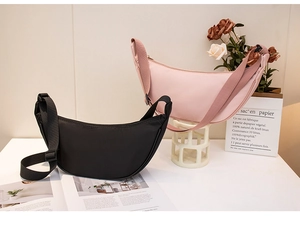Detail view of crescent crossbody bags in pink and black on a minimalist tabletop