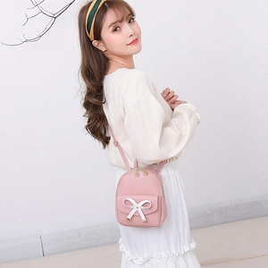 Mini sac à dos rose pour fille avec nœud blanc, présenté par un mannequin en studio