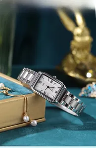 Close-up of square silver steel watch on green velvet background with pearl accents