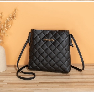 Detail of black quilted crossbody bag with gold metal logo and sleek leather strap