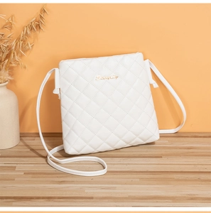 Detail view of a white quilted crossbody bag with golden logo on a warm tabletop