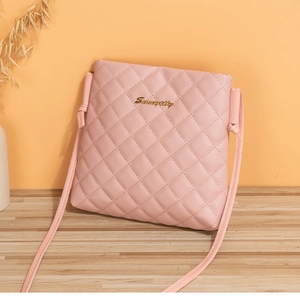 Detailed view of pink quilted crossbody bag with gold logo on a wooden surface
