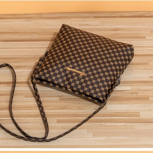 Detail shot of a dark brown crossbody bag with retro pattern and gold hardware on wood