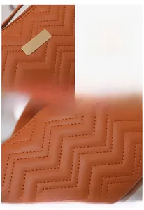 Close-up of brown quilted bag with V-shaped stitching and golden metal hardware detail