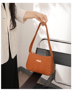Close-up of brown quilted shoulder bag with V-shaped stitching and gold metal detail